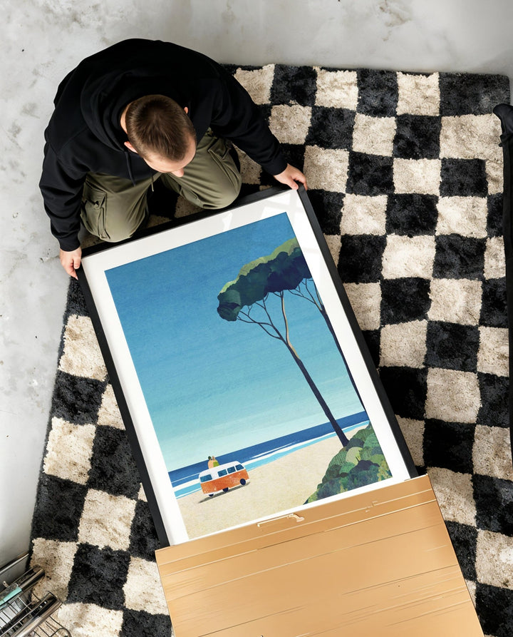 Person holding artwork of a beach scene with a car and tree on a checkered rug.