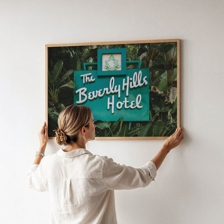 Woman hanging a picture of 'The Beverly Hills Hotel' on a wall.
