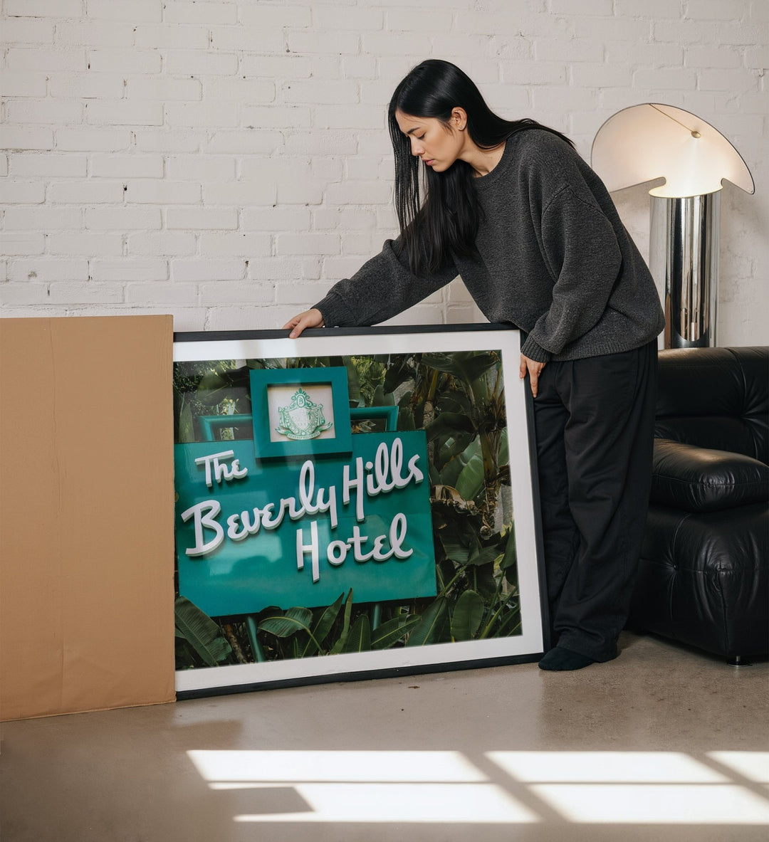 Person holding a picture of The Beverly Hills Hotel sign in a room with a white brick wall.