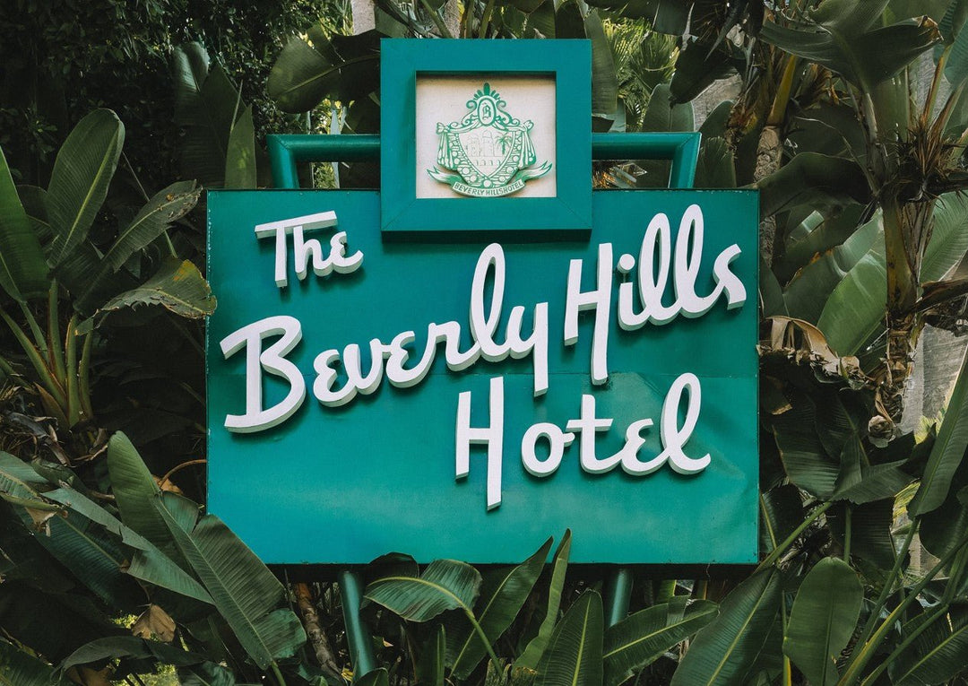Teal sign with 'The Beverly Hills Hotel' text surrounded by green foliage. framed