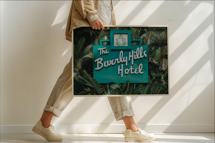 Person holding a picture of 'The Beverly Hills Hotel' with a white wall background