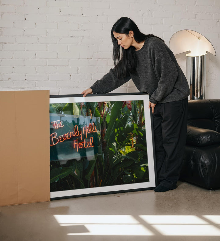 Woman holding a picture of the Beverly Hills Hotel in a living room.