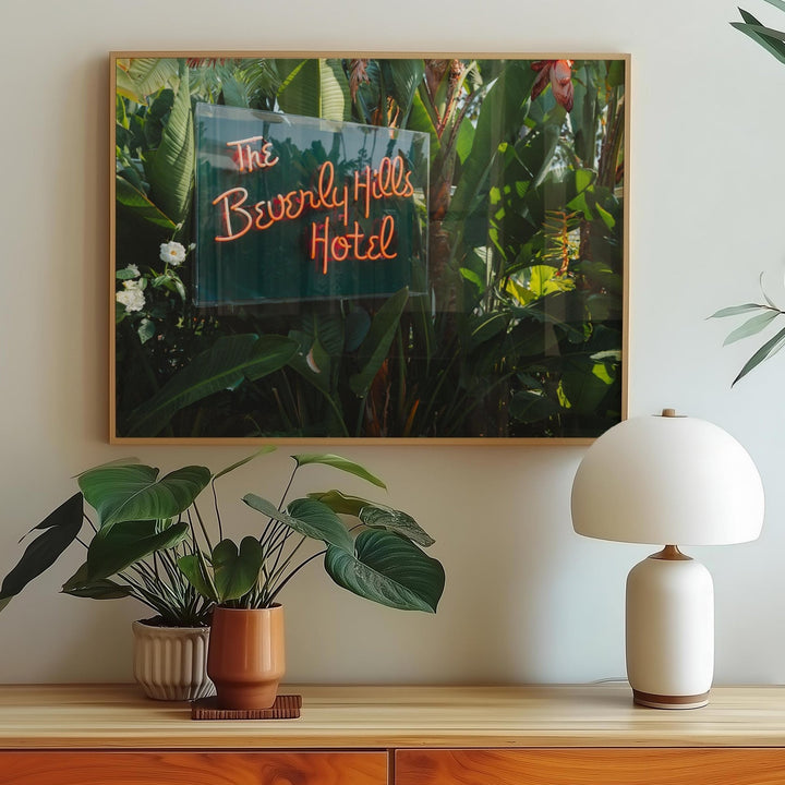 Artwork of the Beverly Hills Hotel sign above a wooden console table with plants and a lamp.