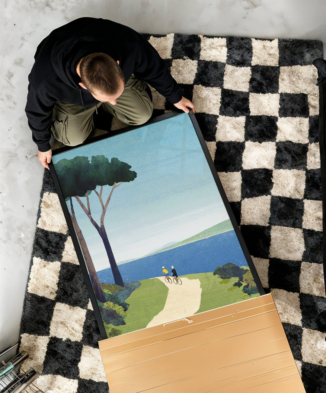Person holding an artwork of a landscape with a checkered rug underneath