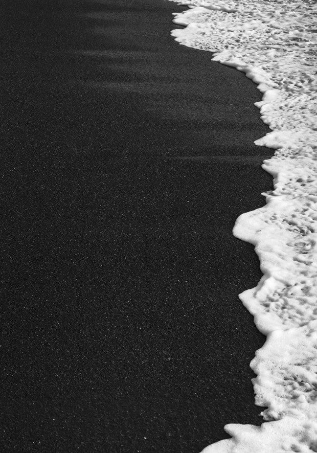 Black sand beach with white foam at the water's edge framed