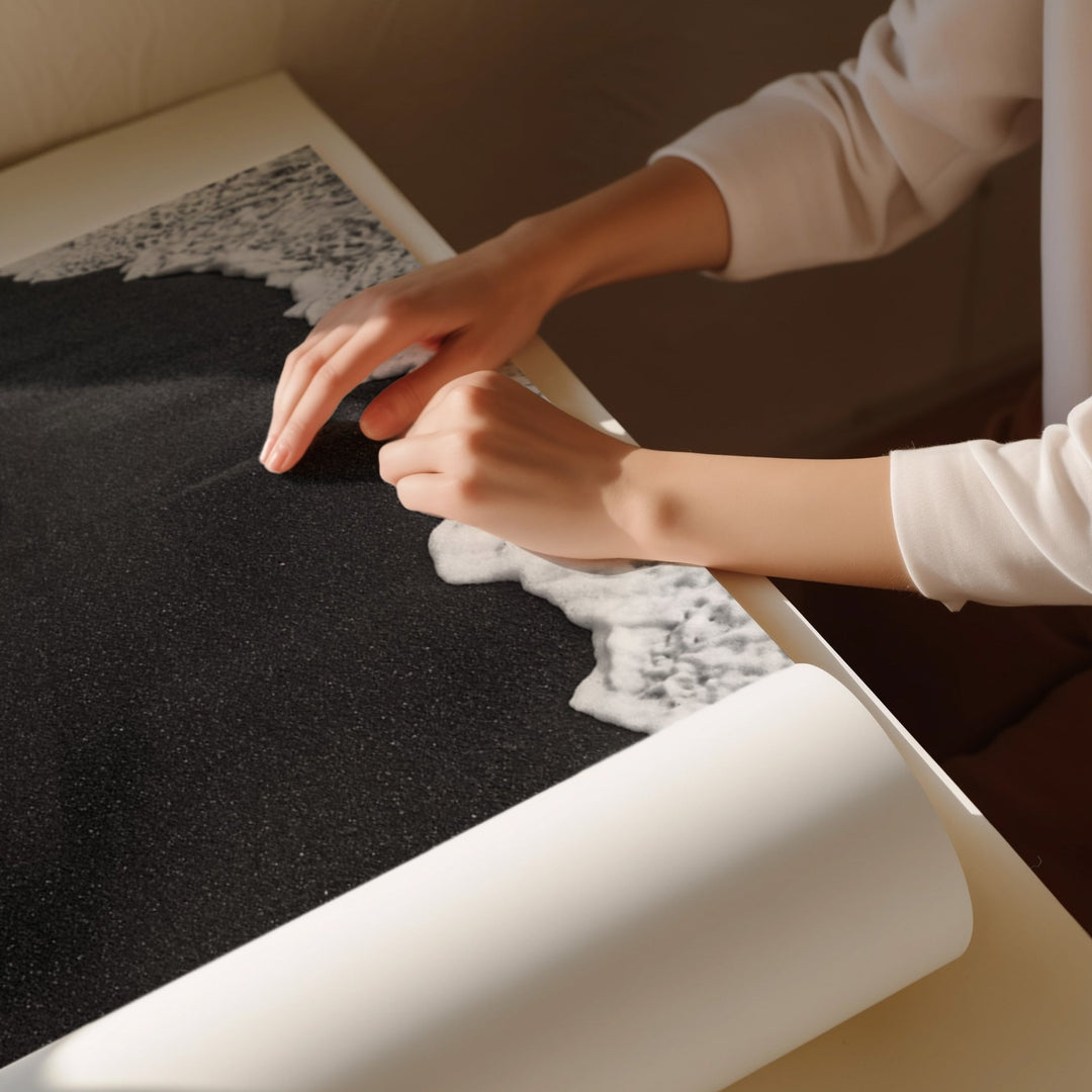 Person unrolling a black carpet with white borders on a wooden floor.