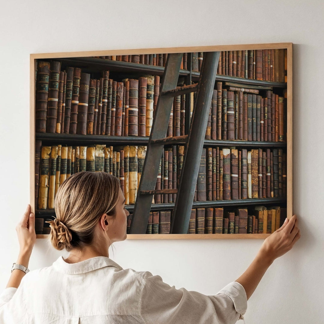 Woman adjusting a picture of a ladder and books on a wall.