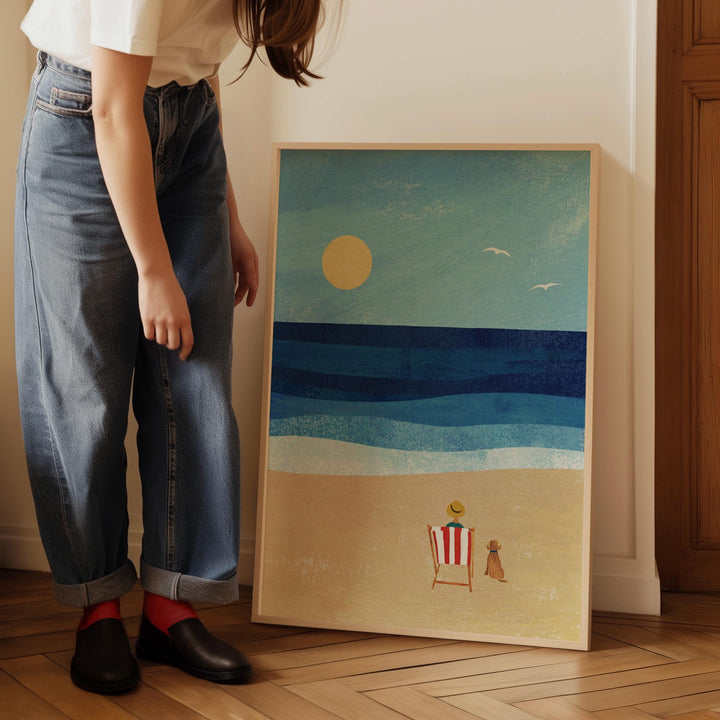 Person standing next to artwork of a beach scene with a sunset.