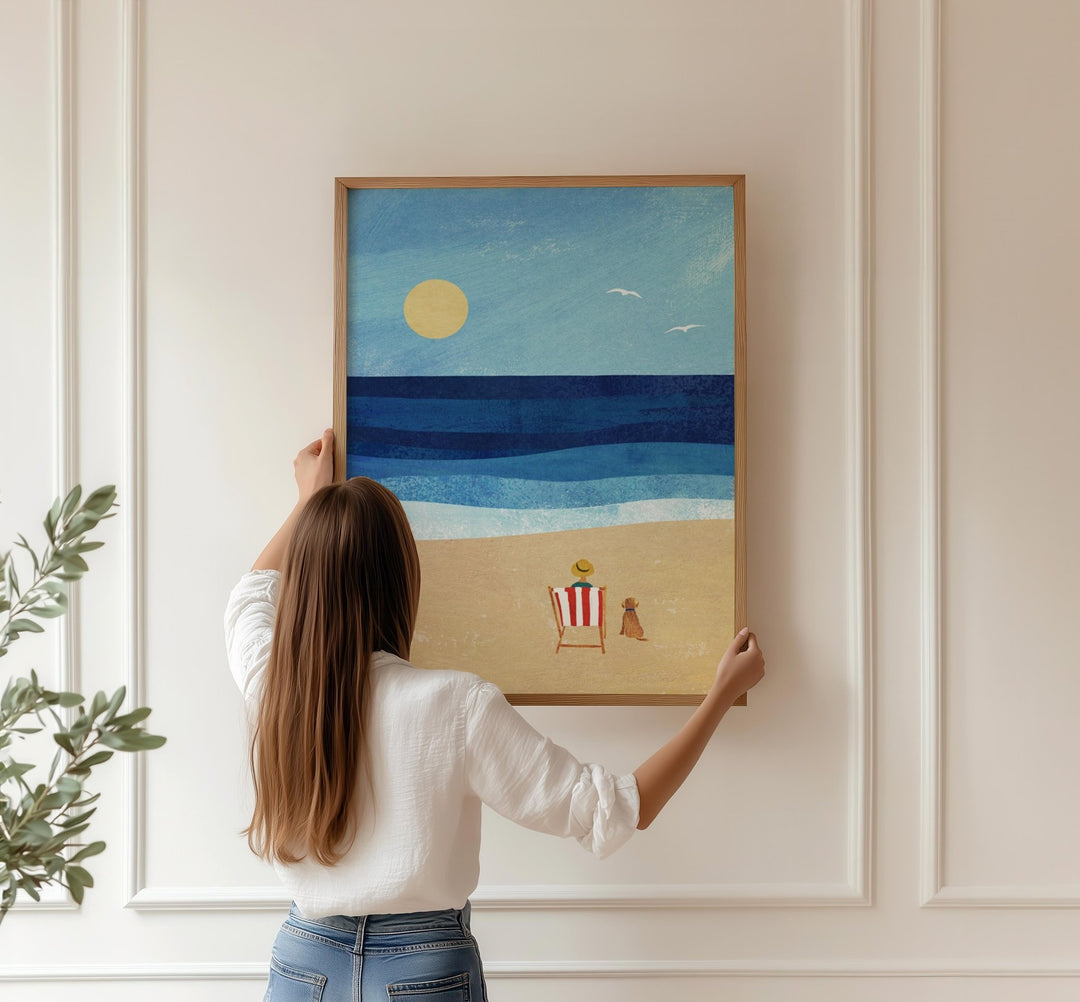 Person hanging an artwork of a beach scene on a wall.