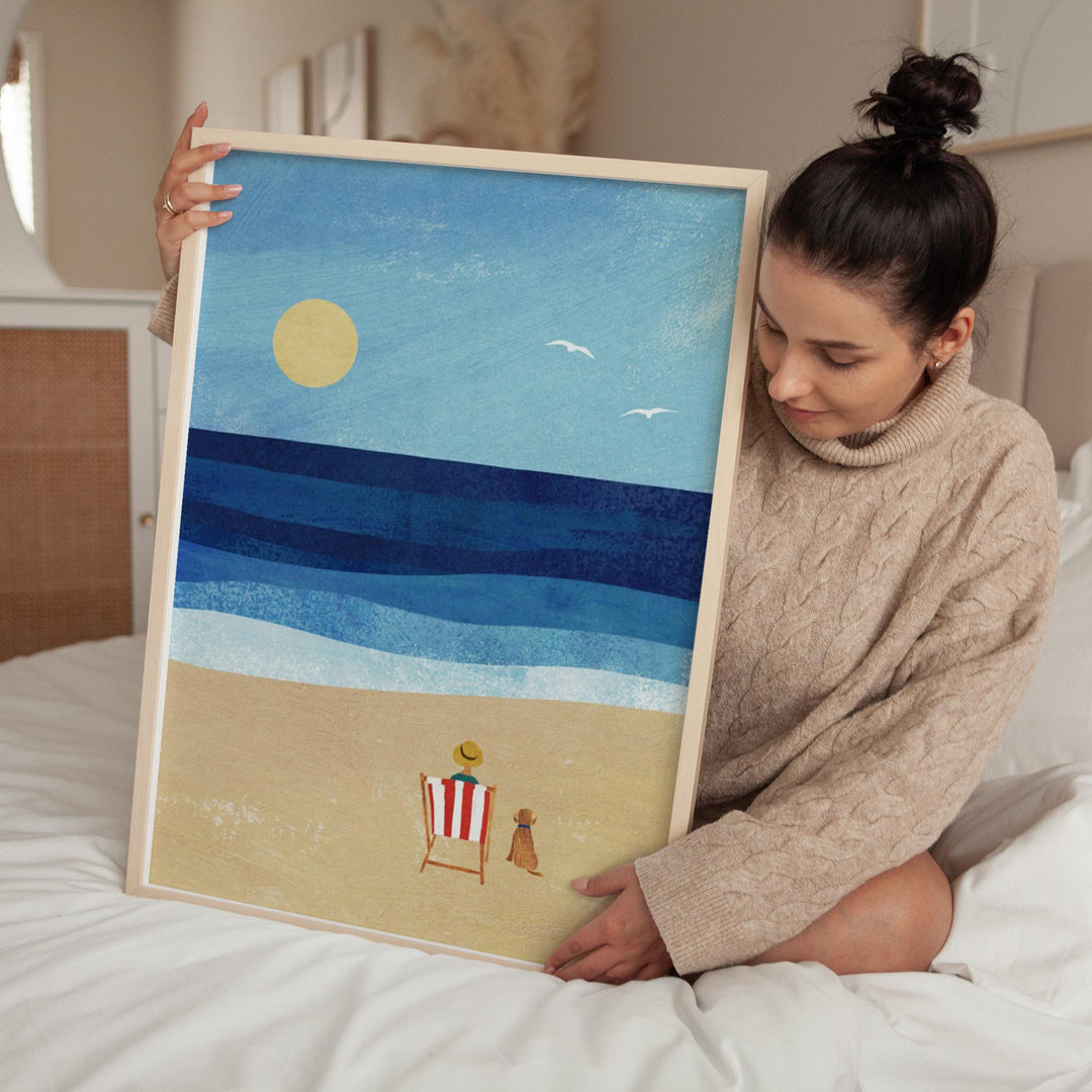 Woman holding artwork of a beach scene with a sun, blue sky, and sand.