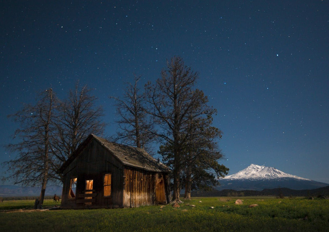 Wooden cabin under a starry night sky with a mountain in the background framed