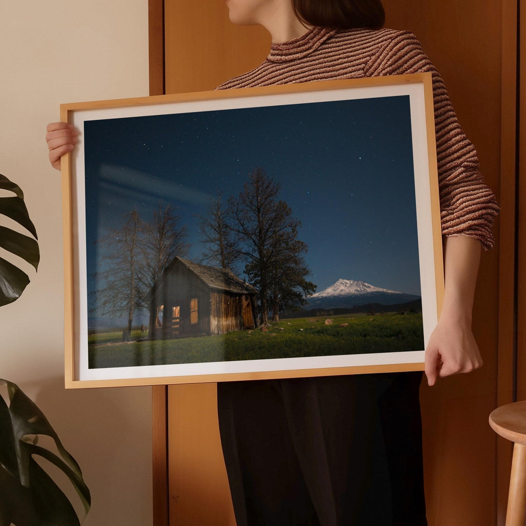 Person holding a photograph of a cabin and mountain landscape.