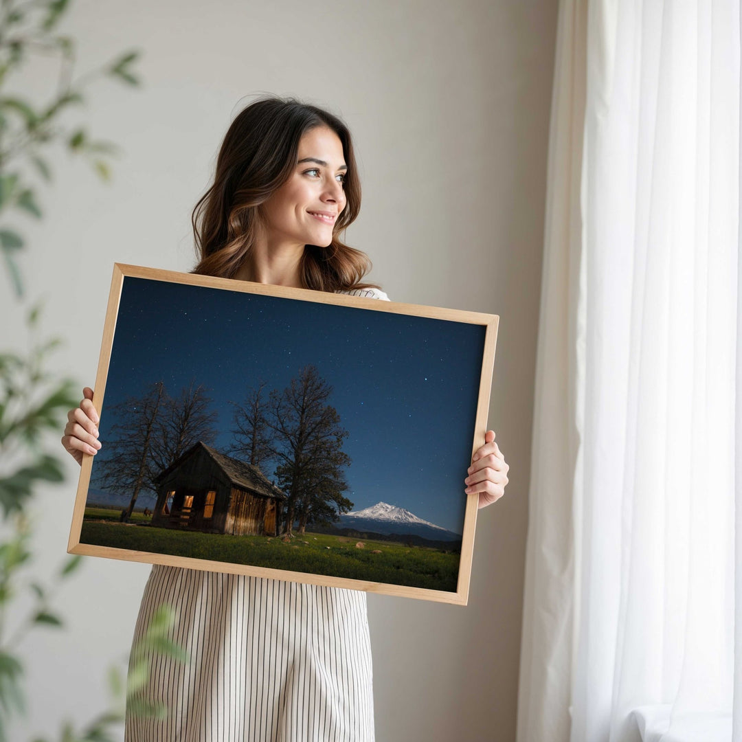 Woman holding a picture of a cabin and mountain at night.