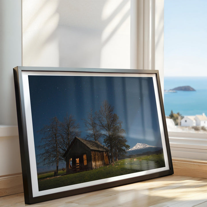 Artwork of a cabin scene with mountains and trees, placed on a surface.