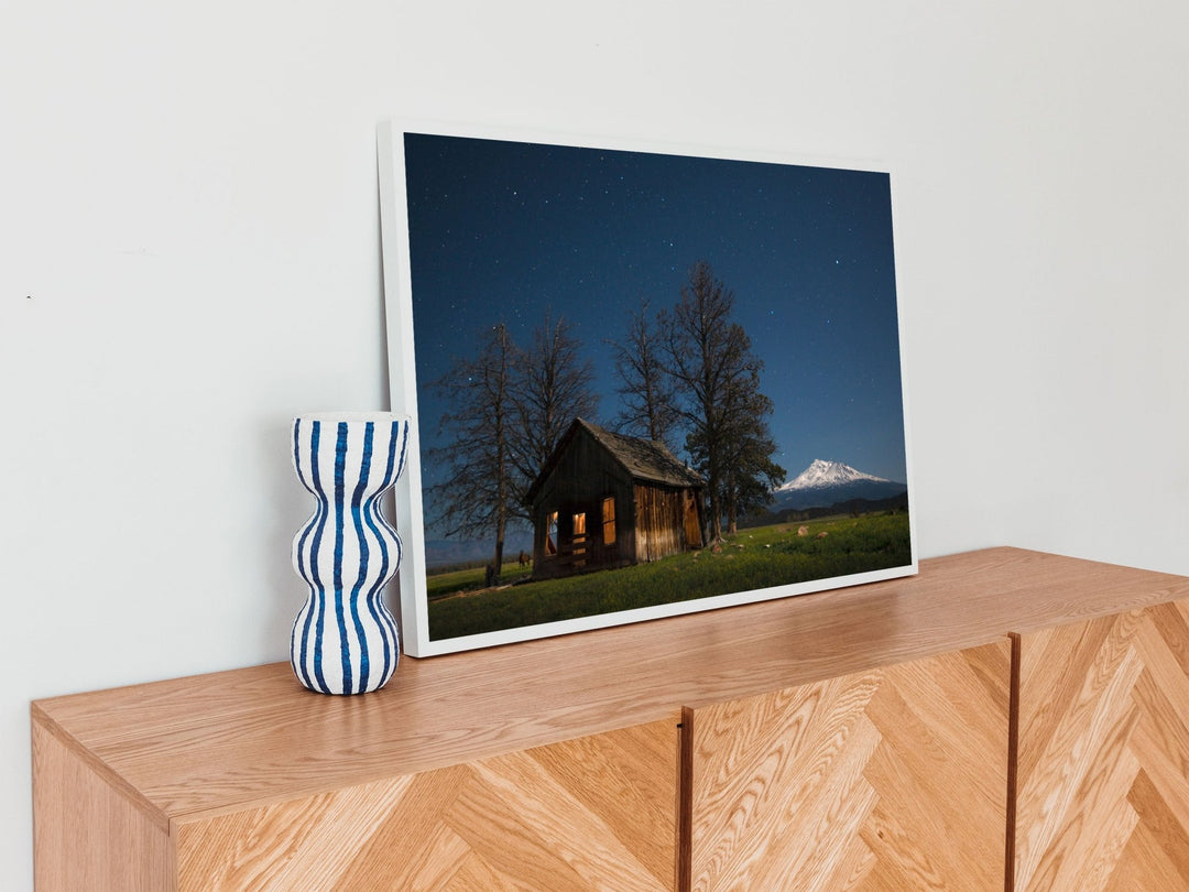 Wooden shelf with a vase and a picture of a cabin in the mountains.