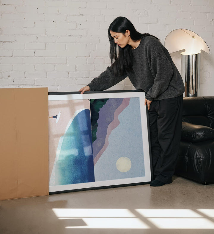 Woman holding an abstract art piece in a room with a white brick wall and a lamp.