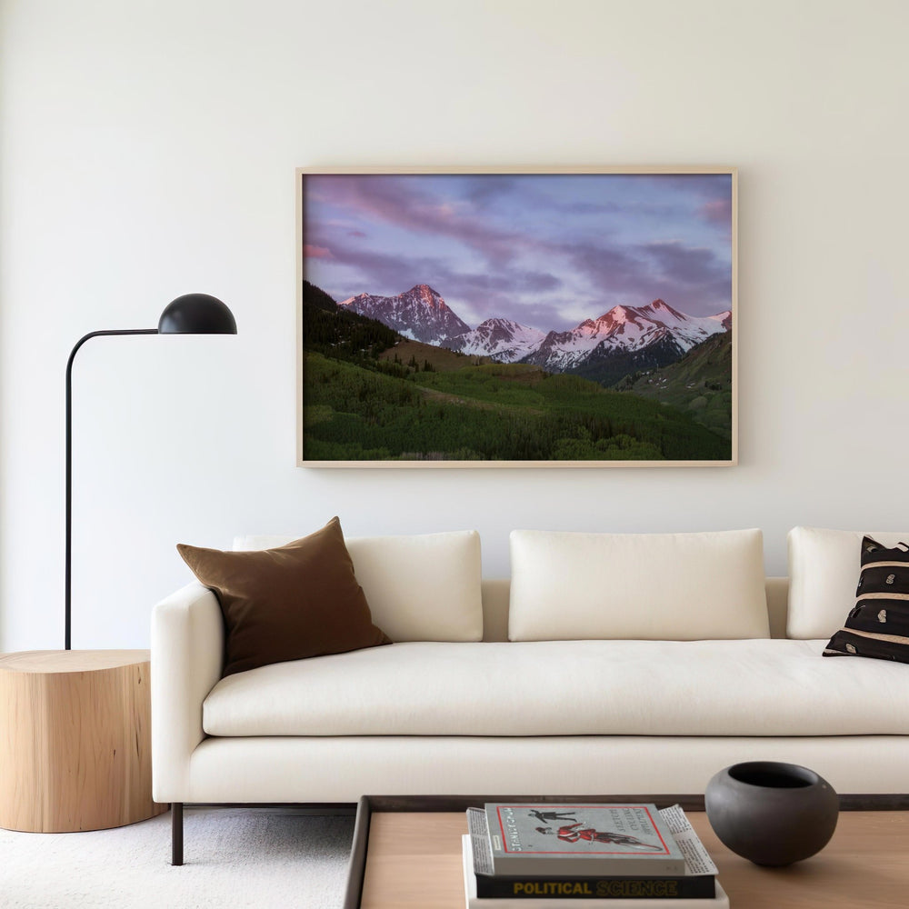 Modern living room with a white sofa, wooden side table, and mountain landscape on the wall.