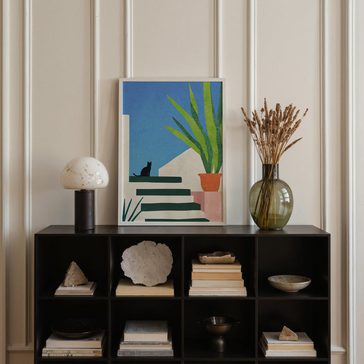 Decorative shelf with books, a vase, and an artwork against a paneled wall.