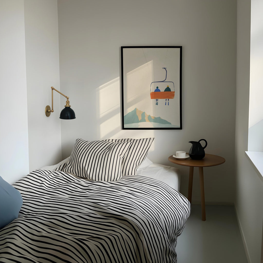 Modern bedroom with striped bedding, side table, and wall art.