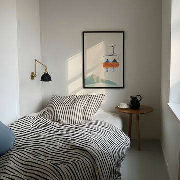Modern bedroom with striped bedding, side table, and wall art.
