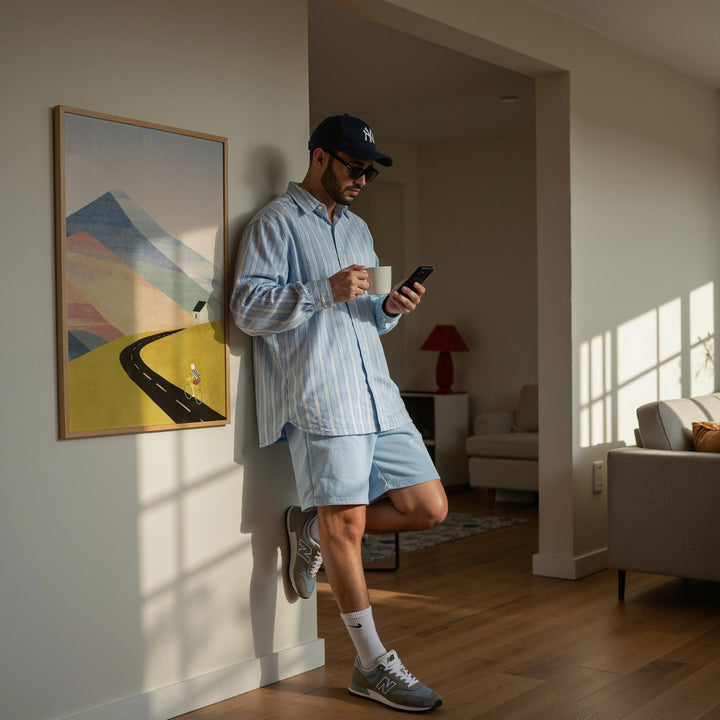 Man in a living room using a smartphone and holding a cup.
