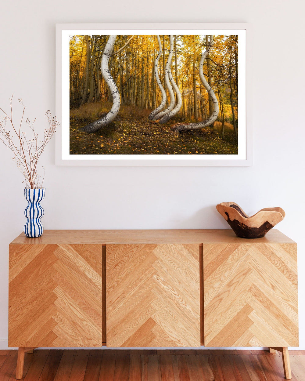 Wooden sideboard with a picture of a forest on a white wall.