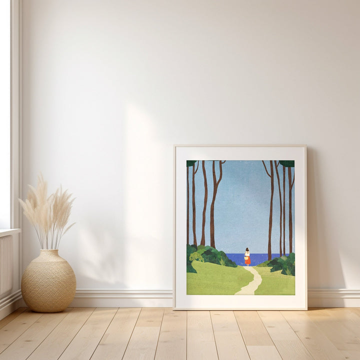 artwork of a woman walking along a path in a forest, placed on a wooden floor with a vase beside it.
