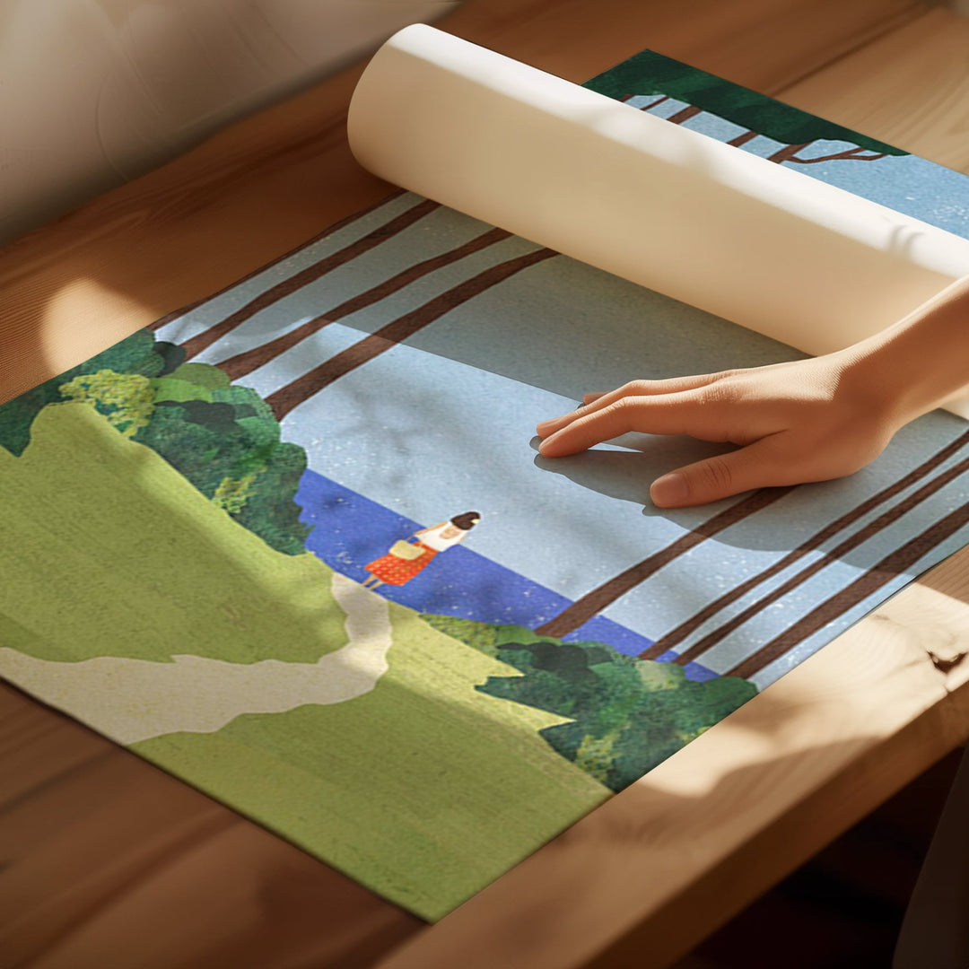 Person rolling out a scenic rug with a landscape design on a wooden floor.