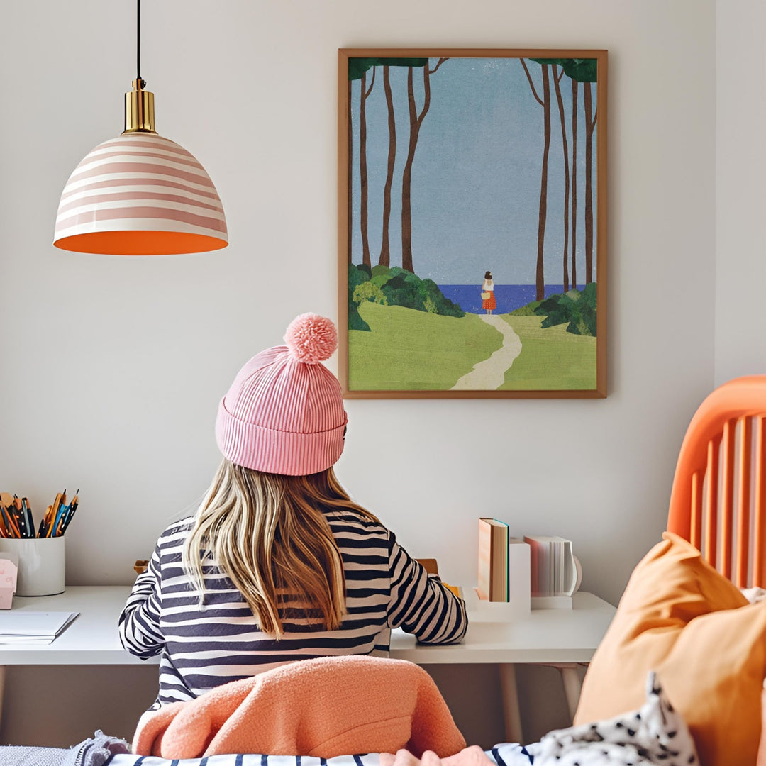 Person wearing a pink beanie sitting at a desk with a painting of a landscape on the wall.