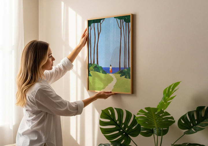 Woman hanging an artwork on a wall with plants in the foreground