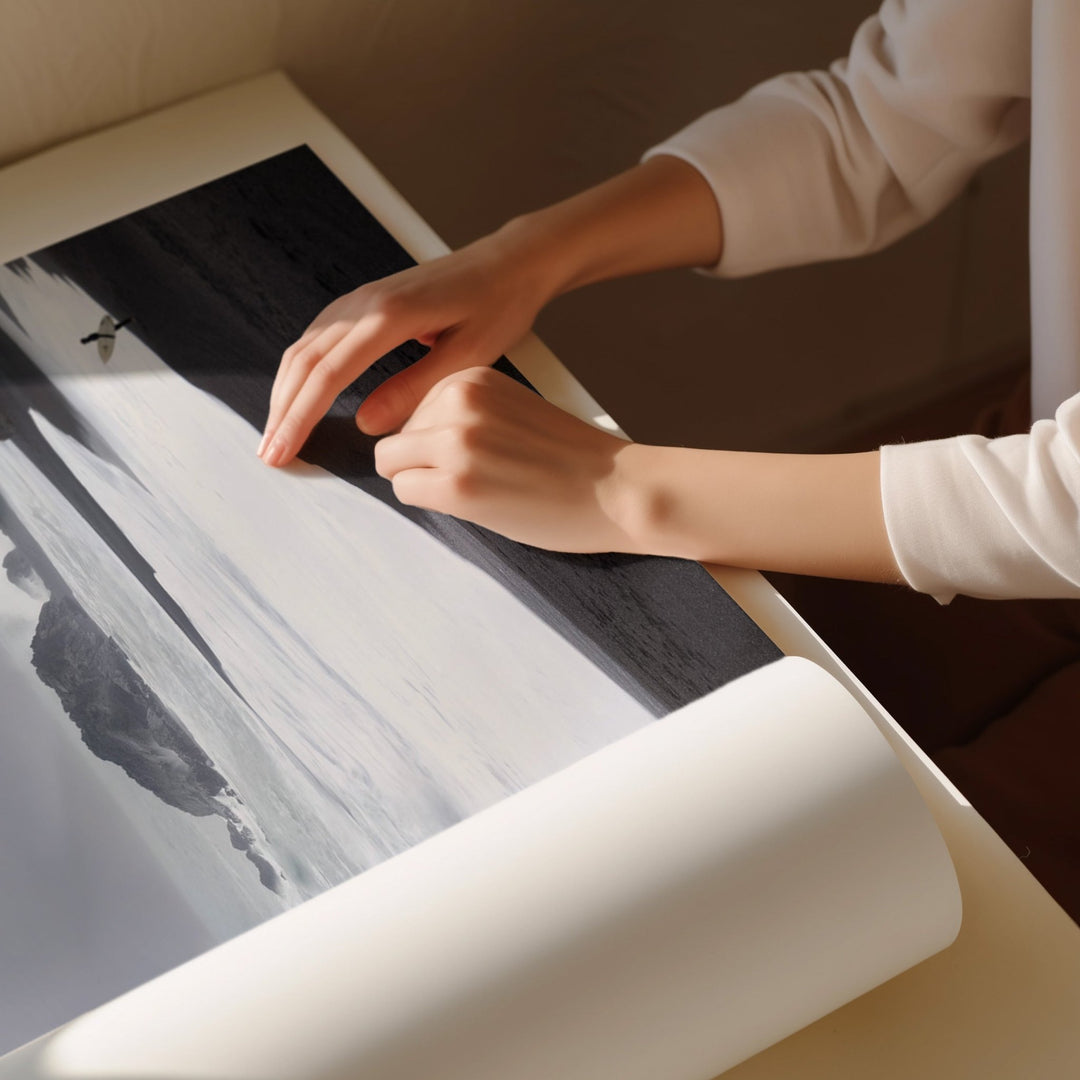 Person rolling out a large piece of paper with a landscape print on a table.
