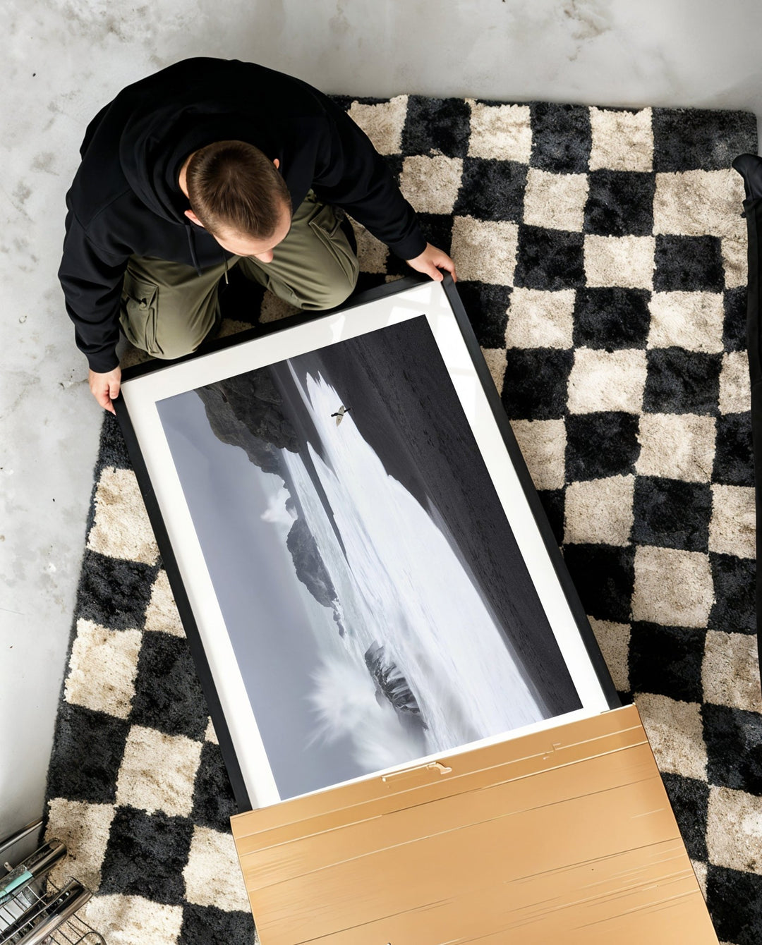 Person unboxing a black and white photograph on a checkered rug.