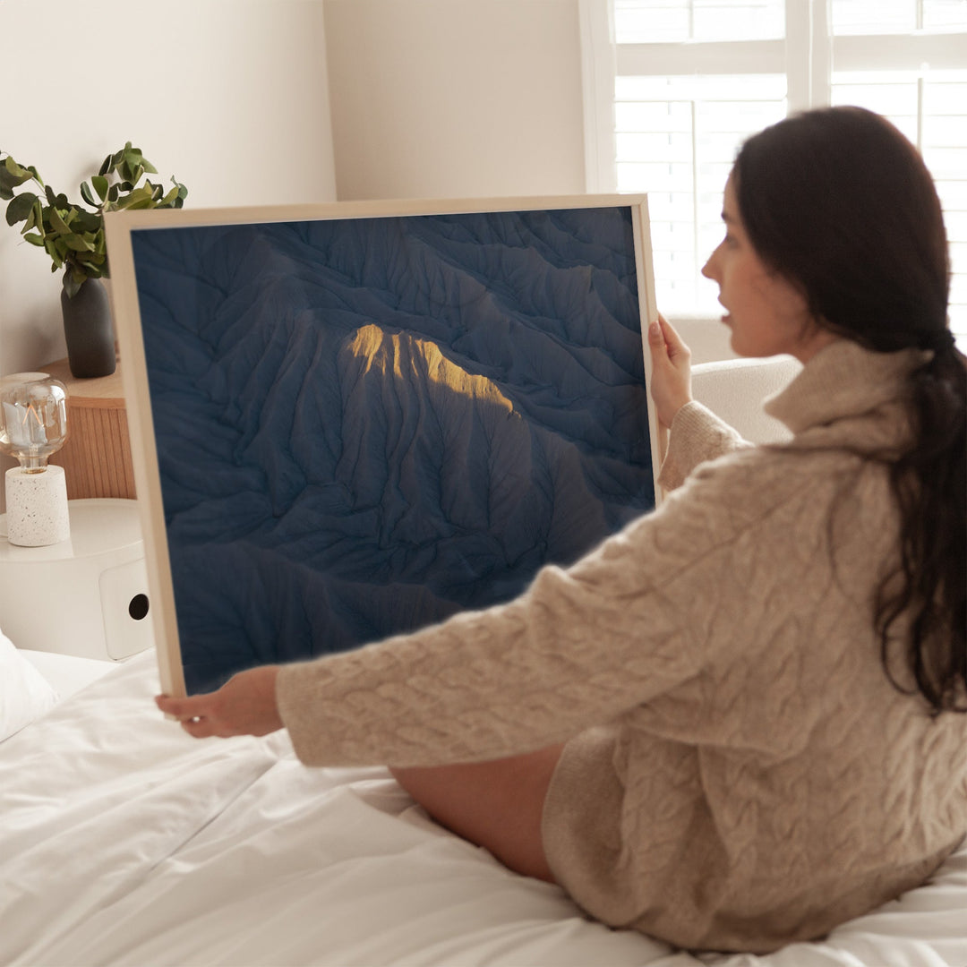 Woman holding a large picture of mountains in a cozy room.