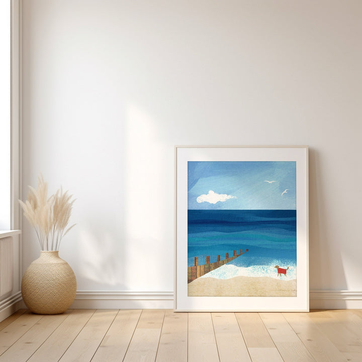 Artwork of a beach scene with a blue ocean and white sky, placed on a wooden floor.