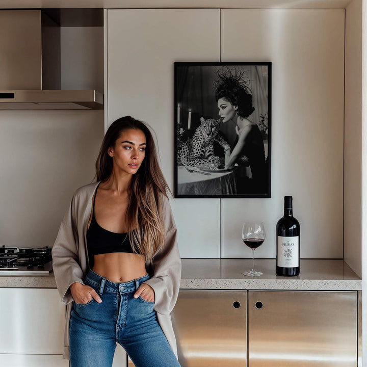 Woman standing in a kitchen with a bottle of wine and a glass on the counter, artwork on the wall.