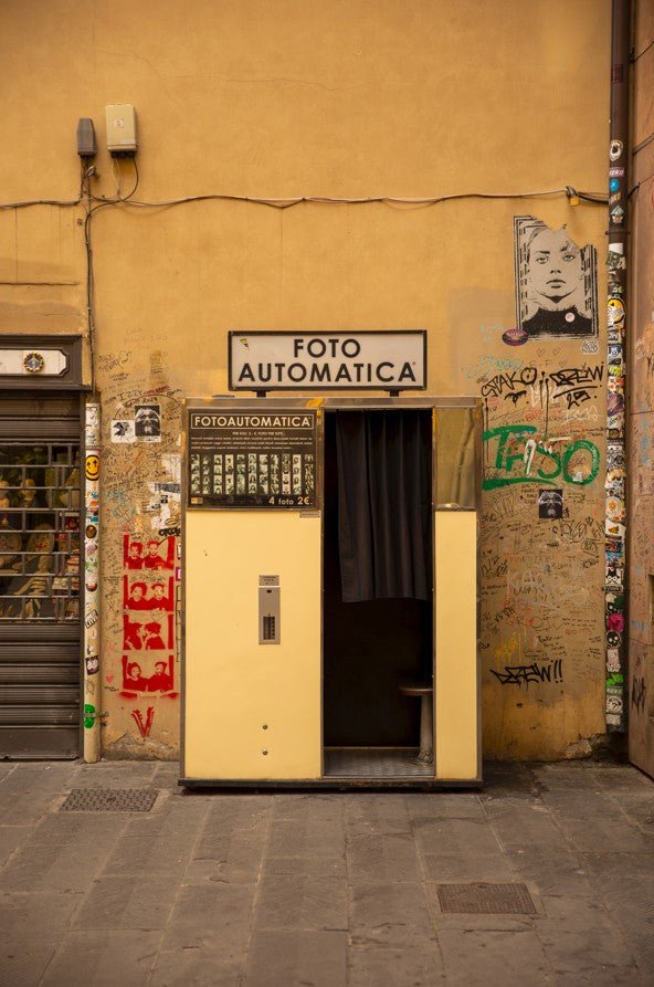 Vintage photo booth with 'FOTO AUTOMATICA' sign on a yellow wall with graffiti. framed