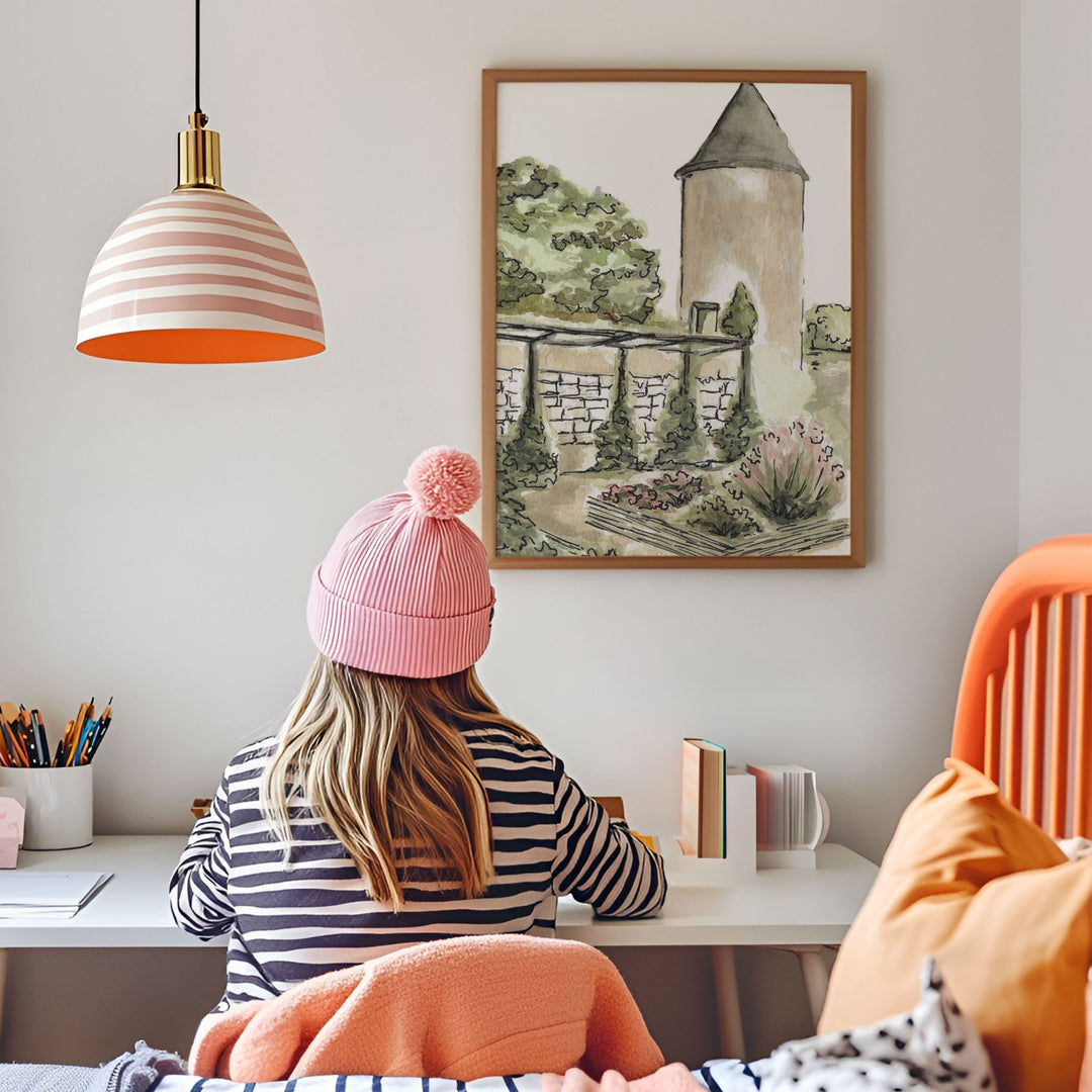 Person wearing a pink beanie sitting at a desk with a painting of a castle on the wall.