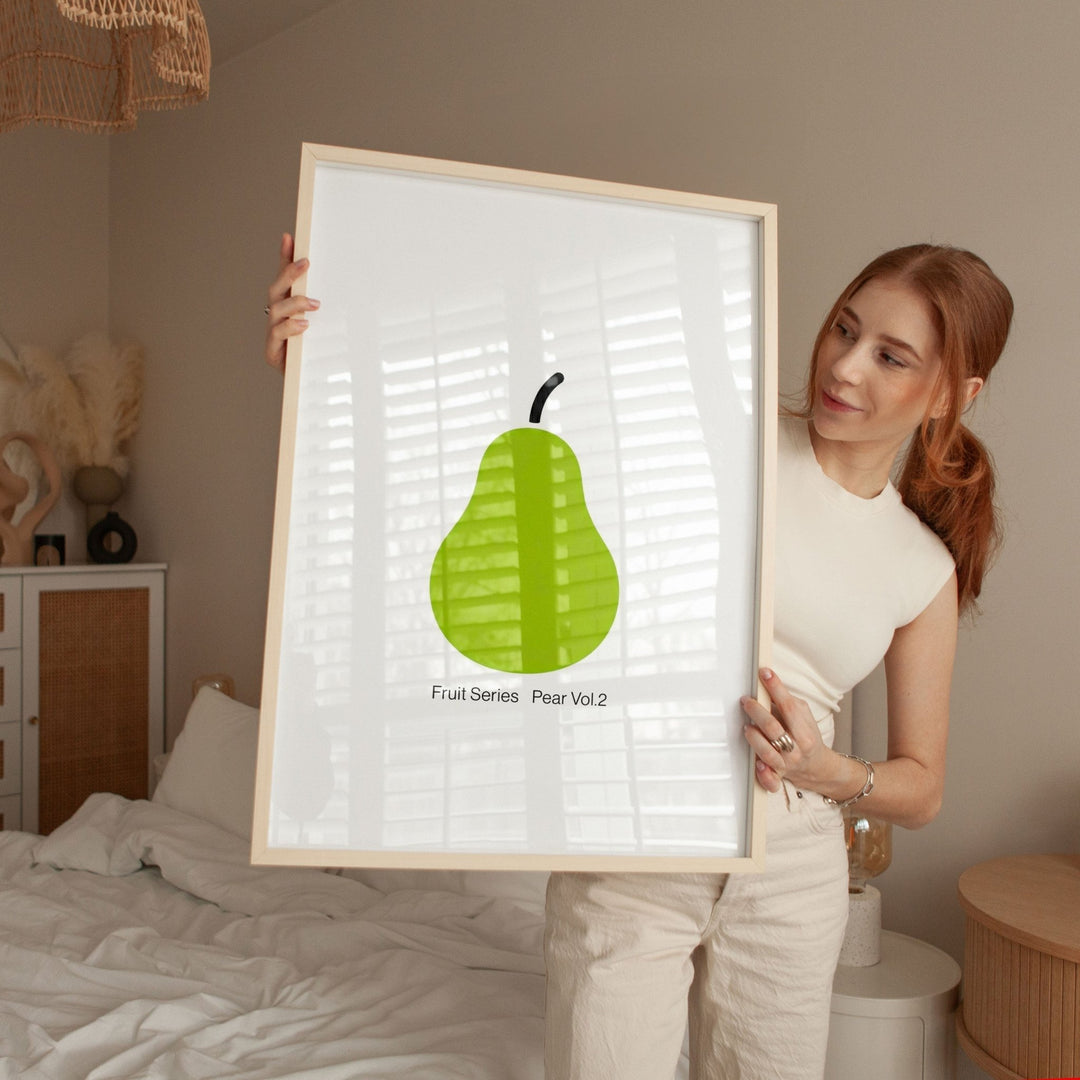 Woman holding a framed print of a green pear in a bedroom setting