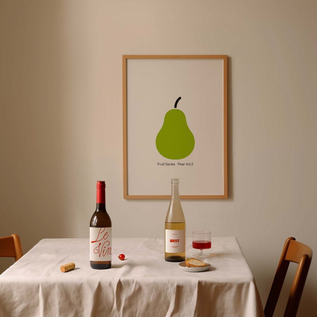 Dining table with wine bottles, a glass of red wine, and a picture of a green pear on a beige wall.