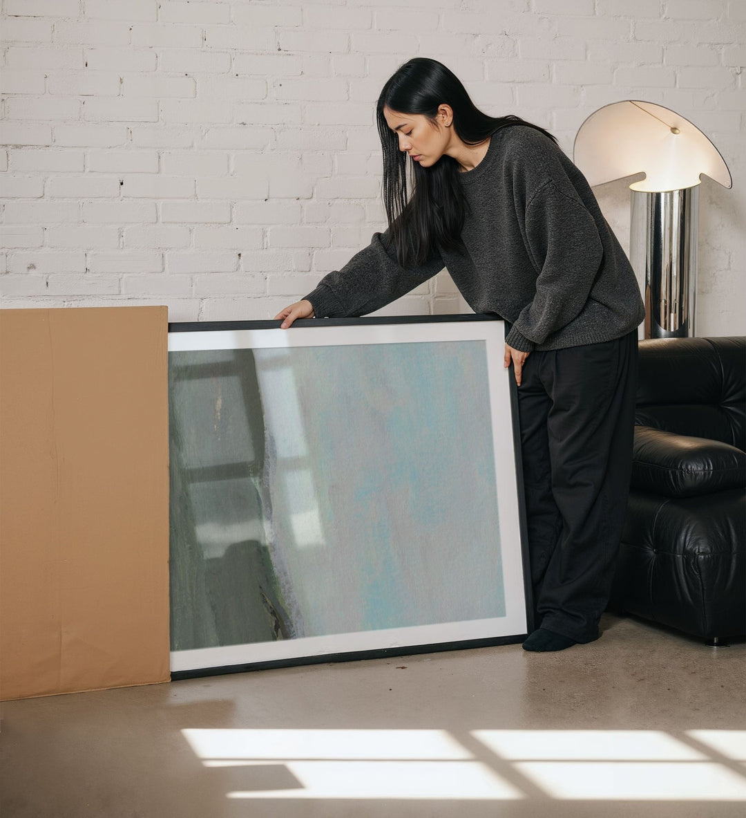 Woman holding a large artwork in a living room.
