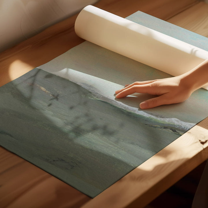 Hand unrolling a large piece of paper with a landscape design on a wooden surface