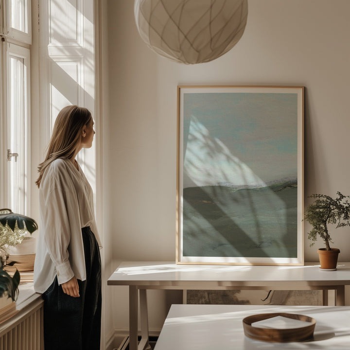 Woman standing by a window in a room with a large picture on the wall.