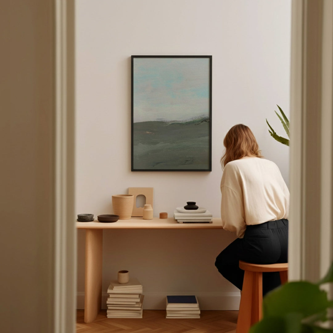 Person sitting at a desk in a home office with a painting on the wall.