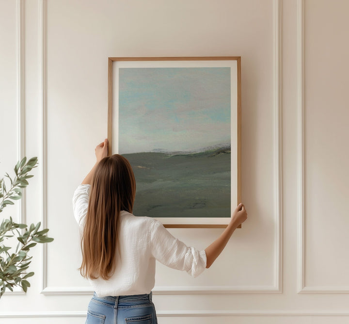 Person hanging a landscape painting on a wall