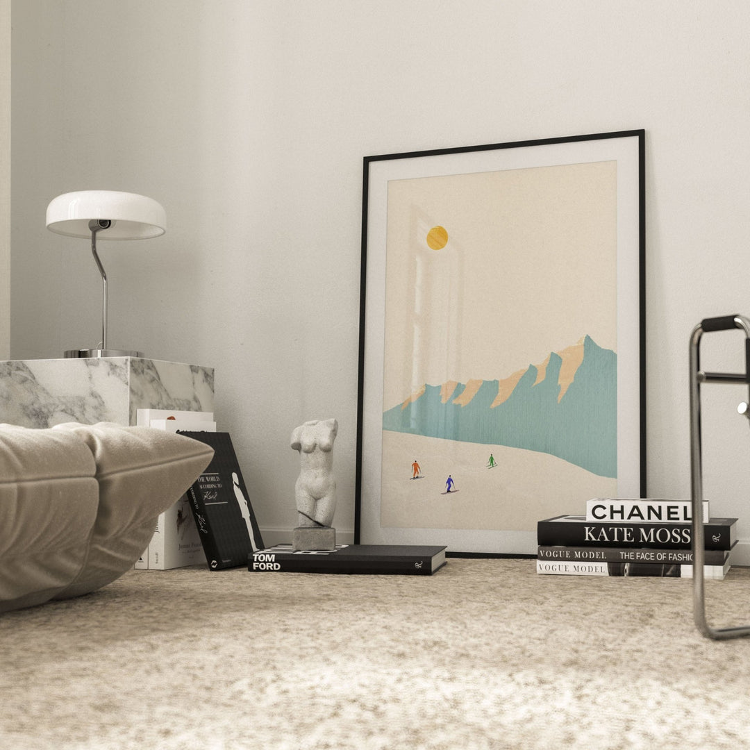 artwork of skiers on leaning on wall with books and sculpture beside it