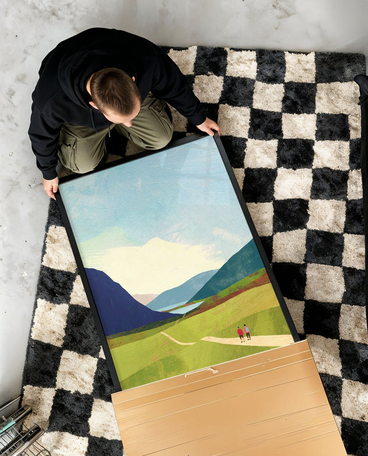 Person unboxing a landscape painting on a checkered rug.