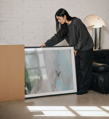 Woman holding a large picture in a living room.