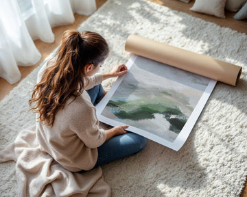 Woman unrolling a large landscape painting on a carpeted floor.