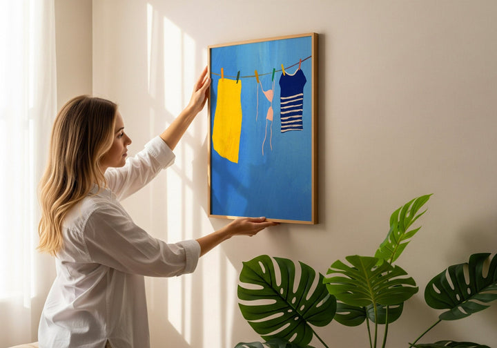 Woman hanging a artwork of clothes on a line against a white wall.