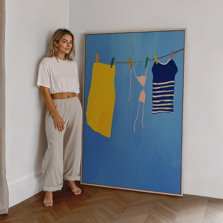 Woman standing next to a large painting of clothes on a line against a white wall.